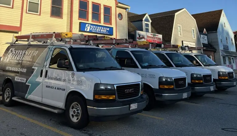 Four Sylvester Electric service vans parked beneath the company sign