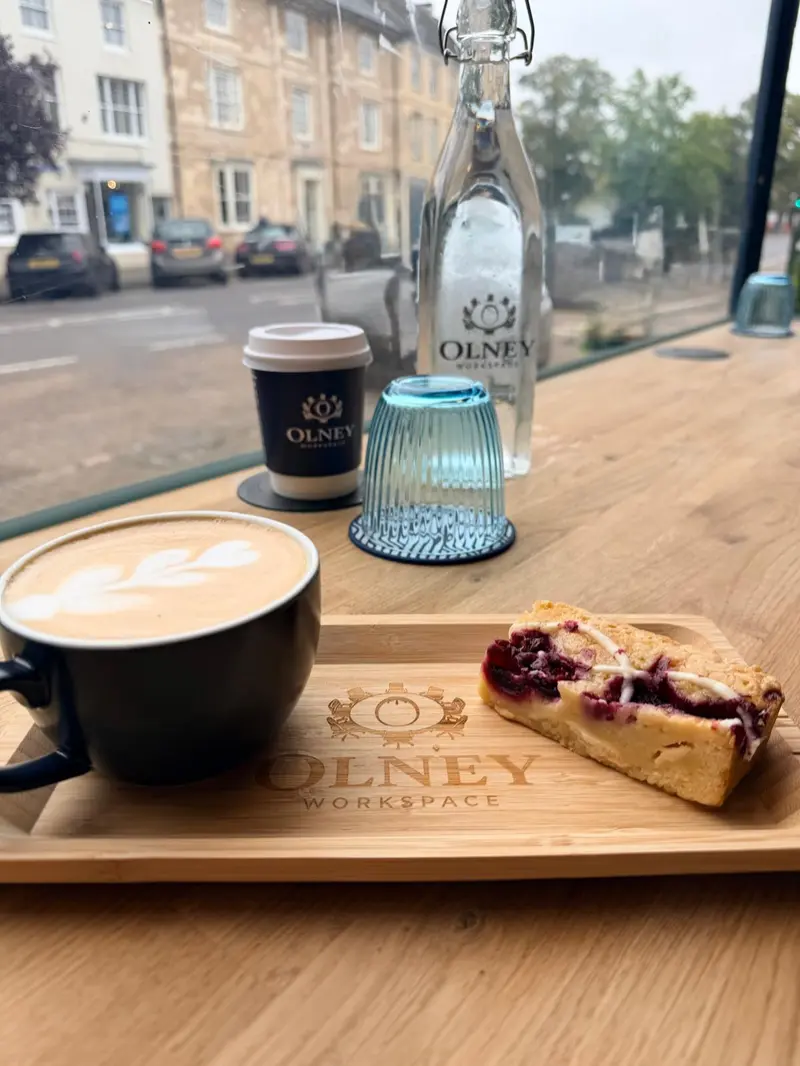 A latte, cake and an Olney Workspace bottle in the window, looking out over Olney High Street
