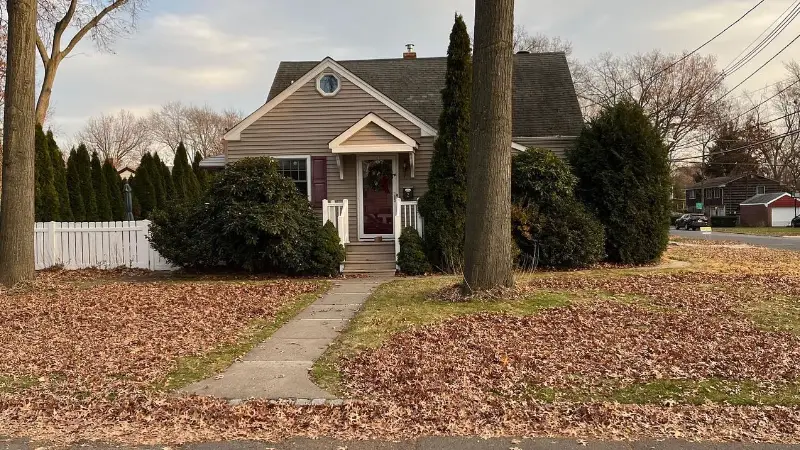 Front yard of a cape-style house covered in leaves