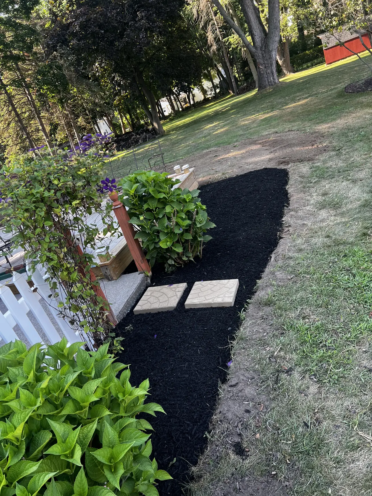 New black mulch bed with stepping pavers beside a white fence