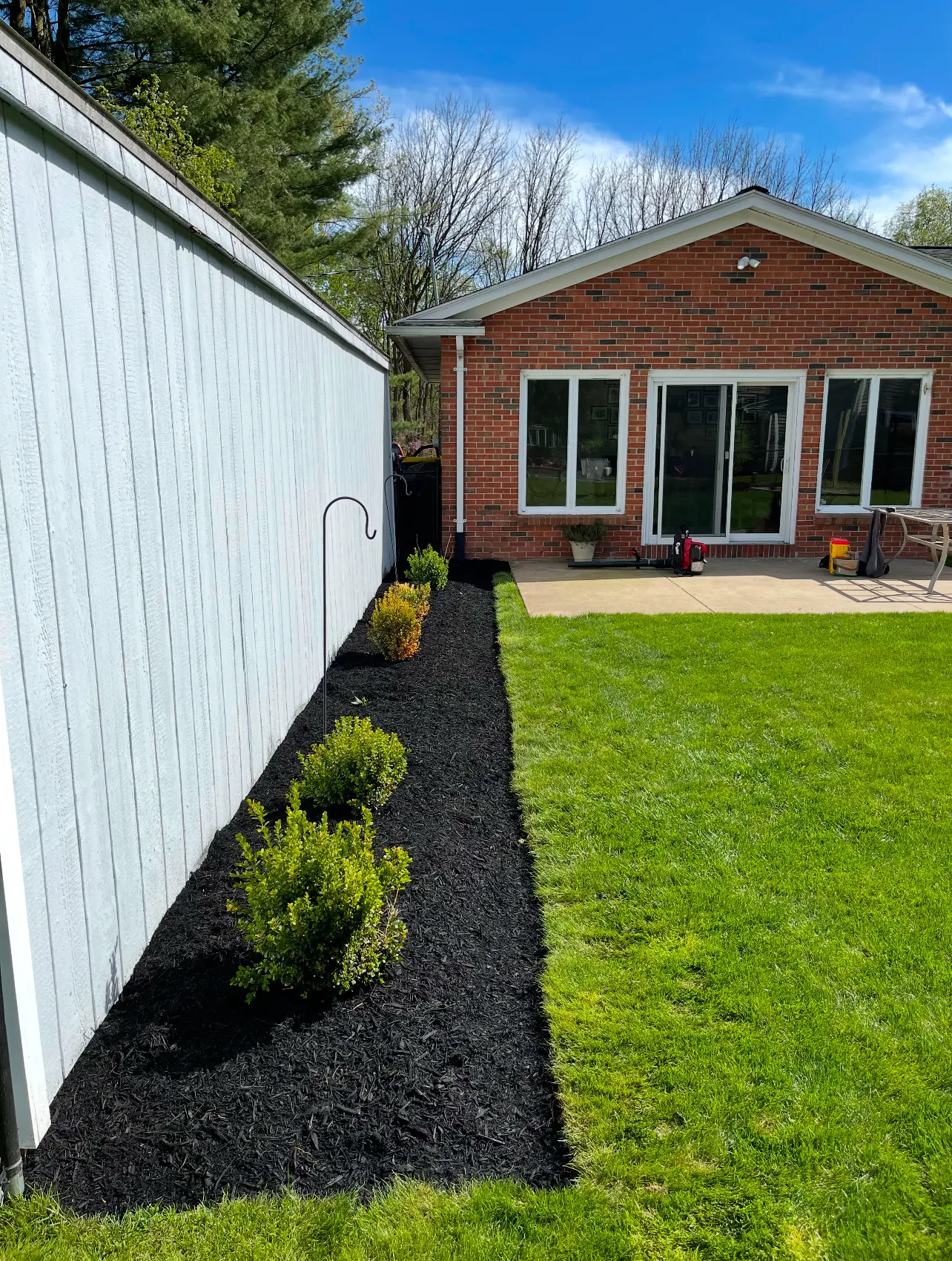 Same bed rebuilt with black mulch, shrubs and a curved edge