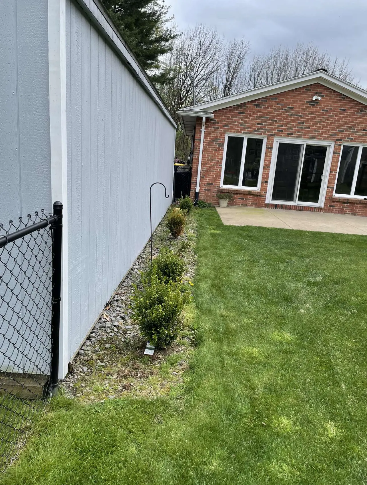 Narrow bed along a garage wall with sparse stone and weeds