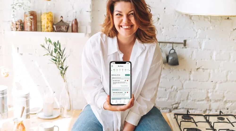 Woman in a kitchen holding a phone displaying a personalised menu