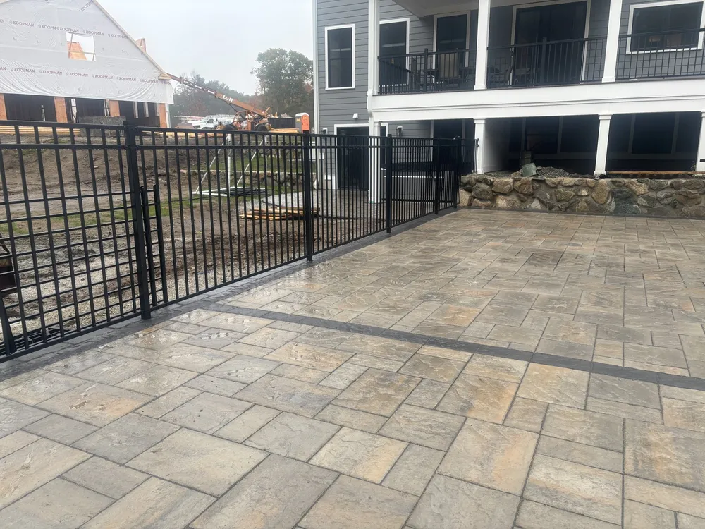 Black aluminum fence around a new stone patio by All Fenced In