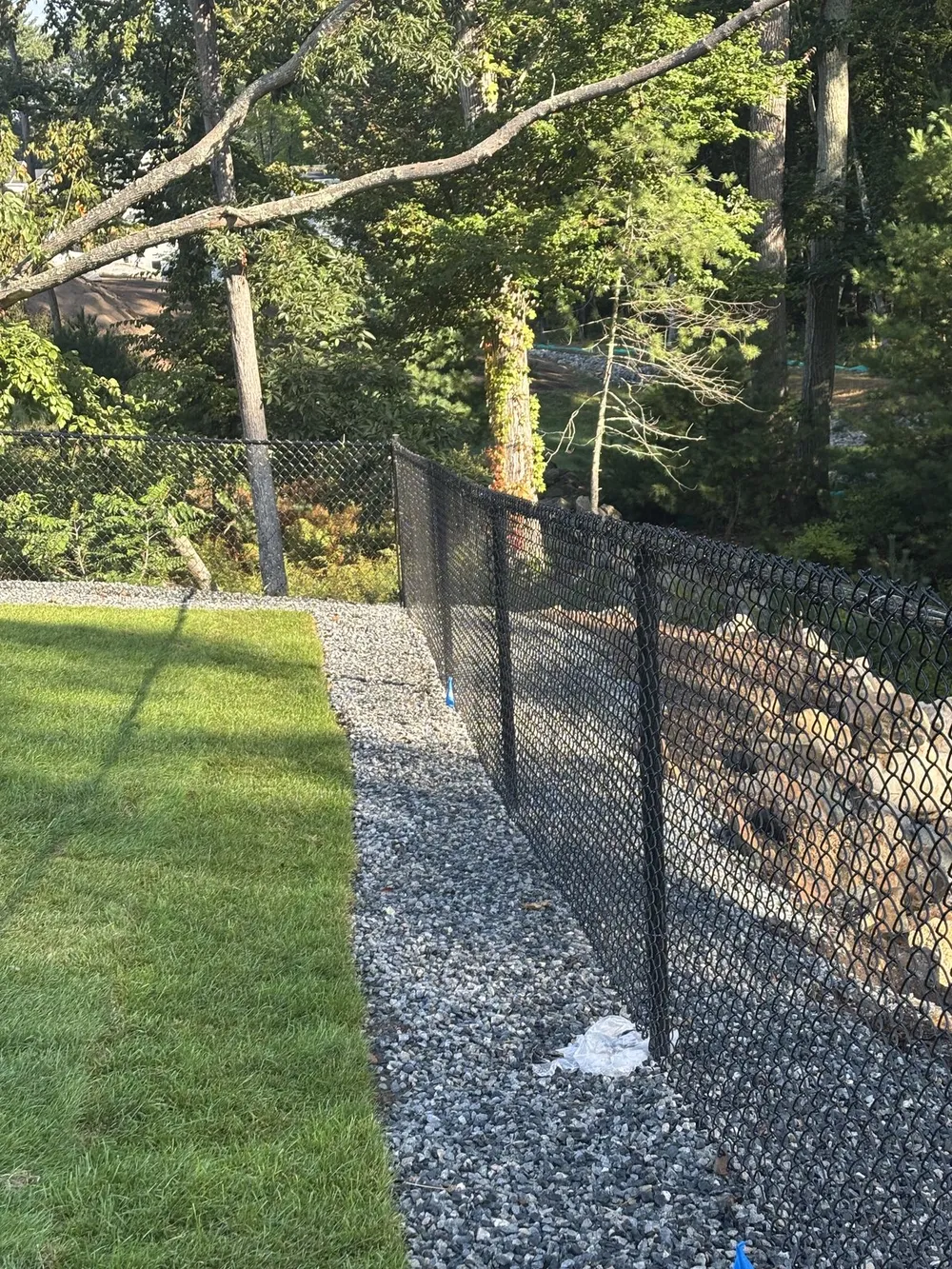 Black chain link fence along a wooded property line by All Fenced In