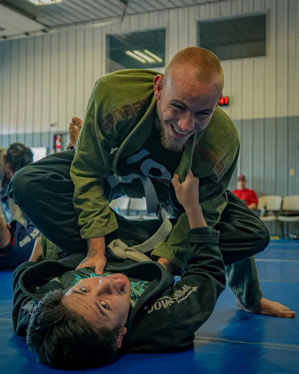 Two training partners smiling mid-roll during an adult jiu-jitsu class