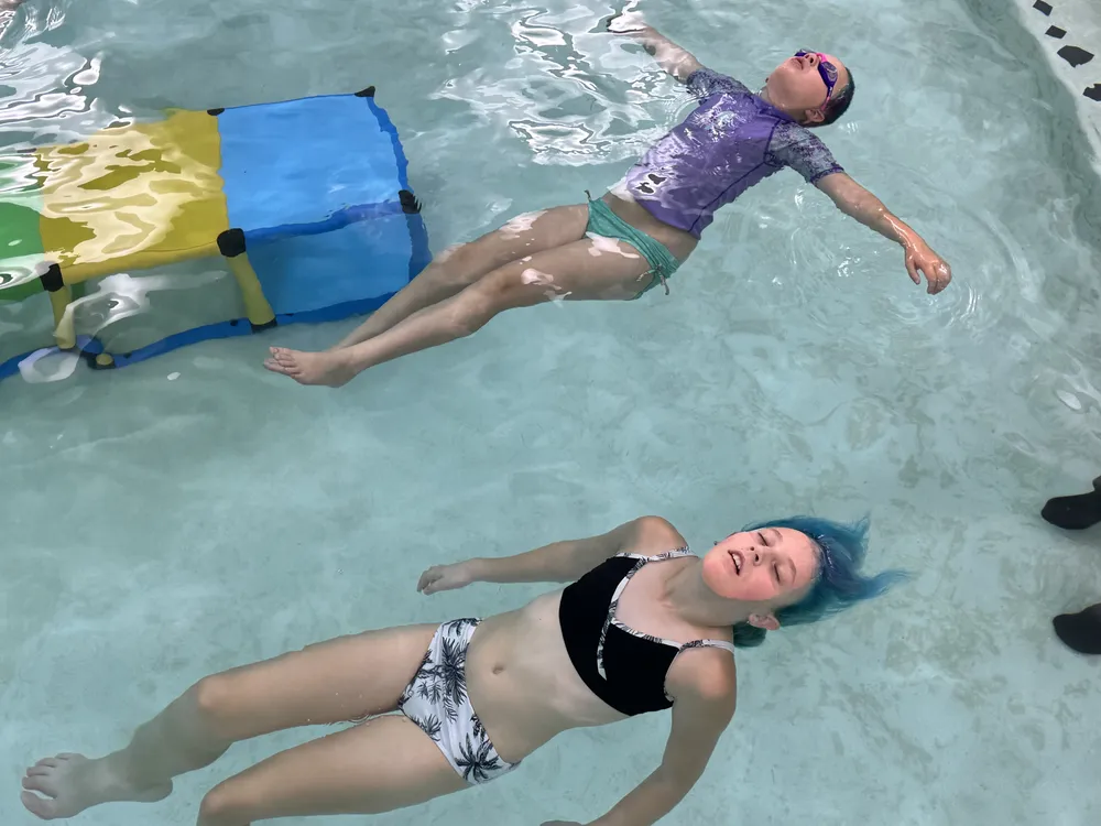 A swimmer floats on their back with a coach's hands under them