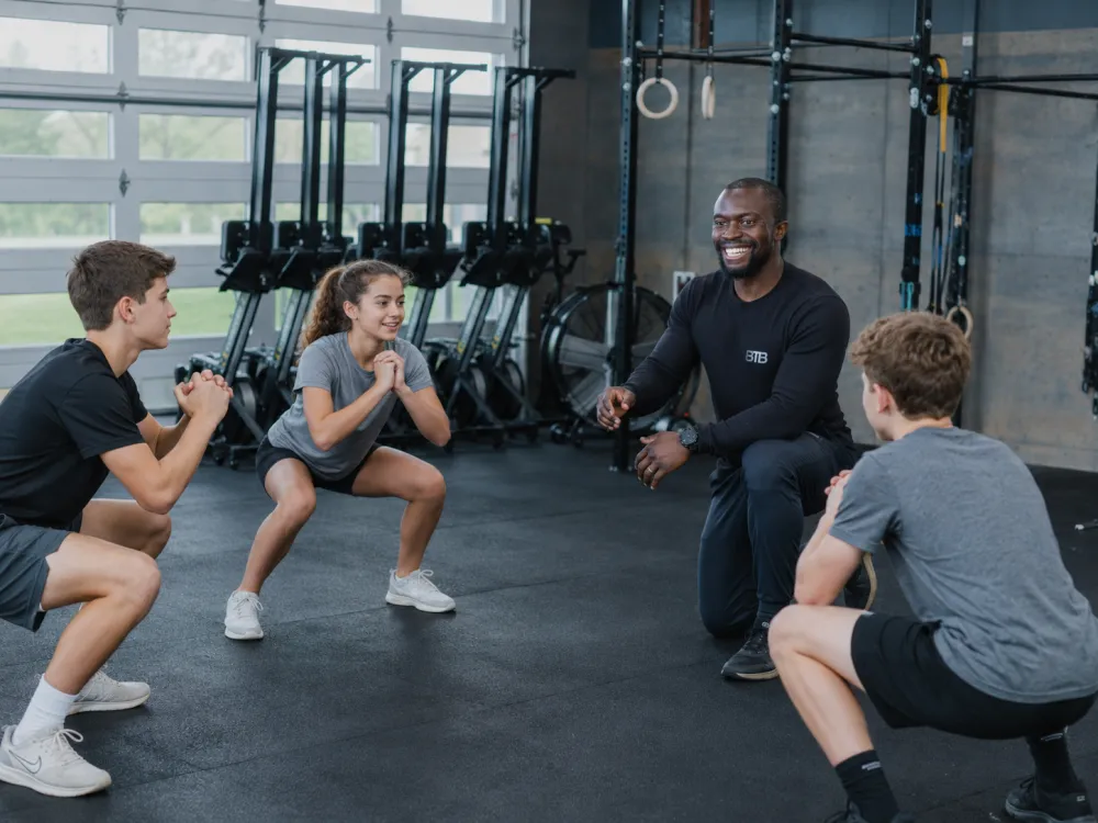 Coach Myles Cornwall coaching three teenage athletes through squats