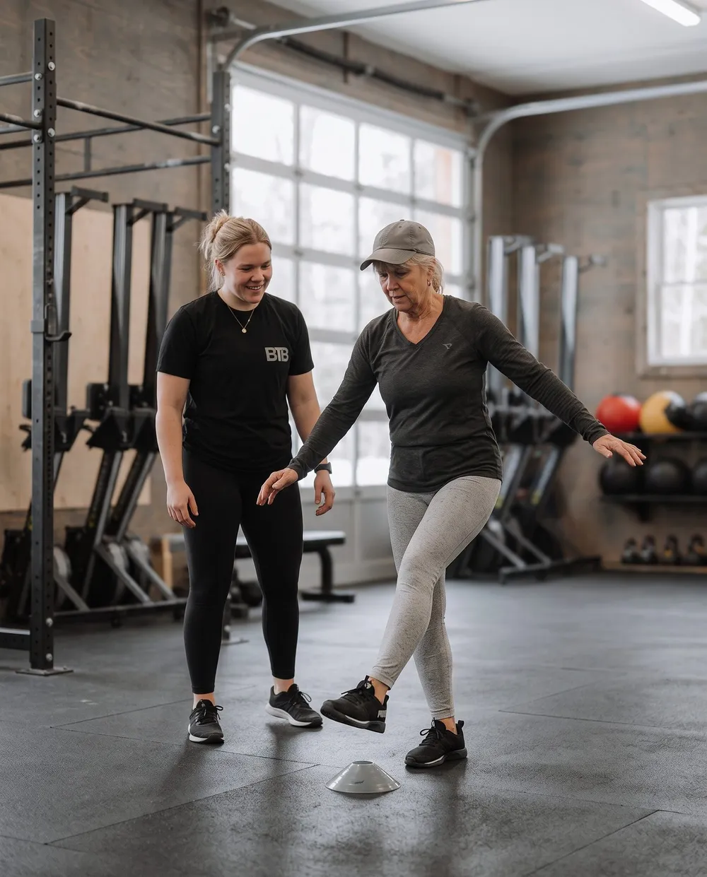 A coach guiding a woman through a stepping balance drill at Between The Bumpers