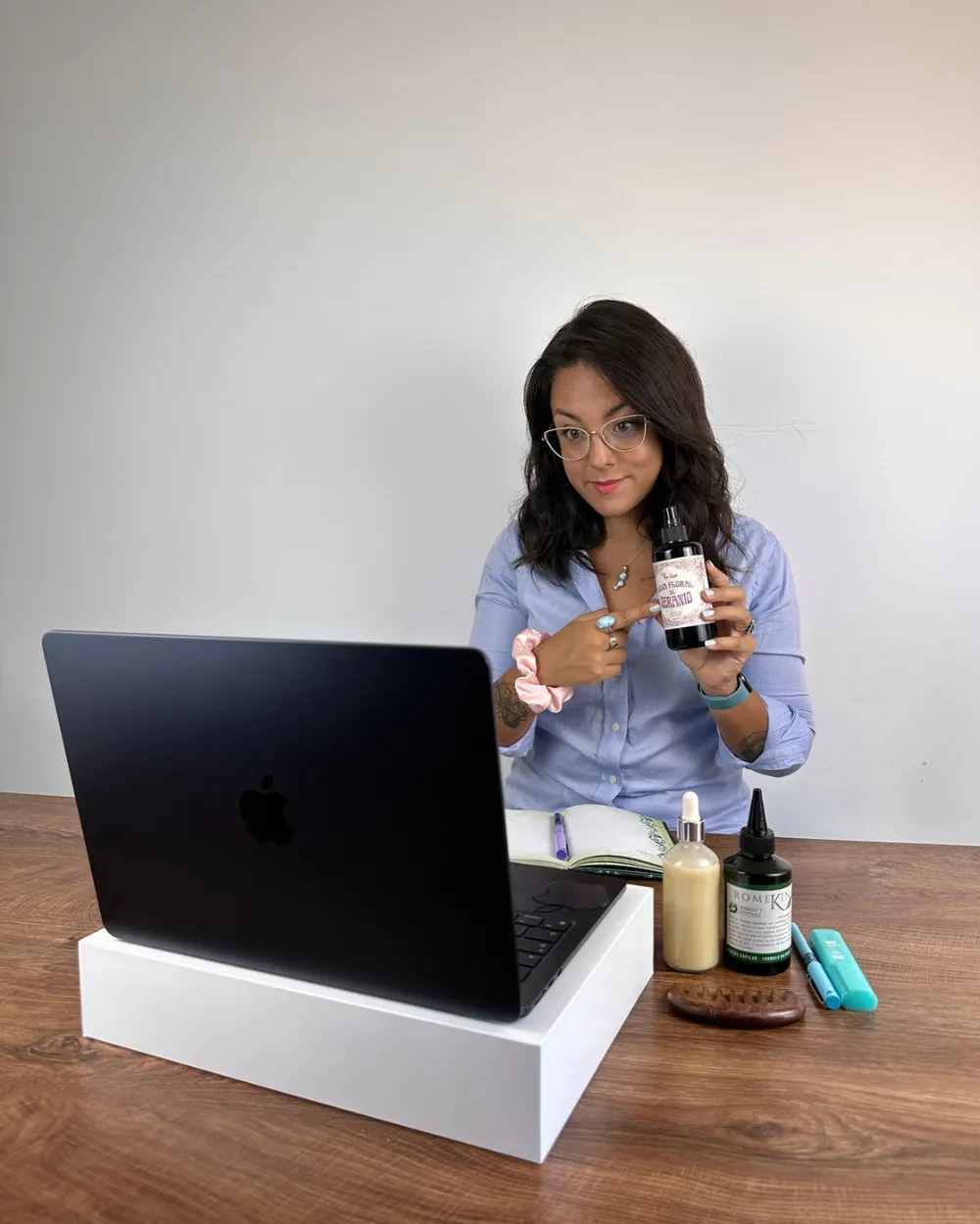 Lesly en su mesa de trabajo, frente al ordenador, enseñando un frasco de tónico capilar