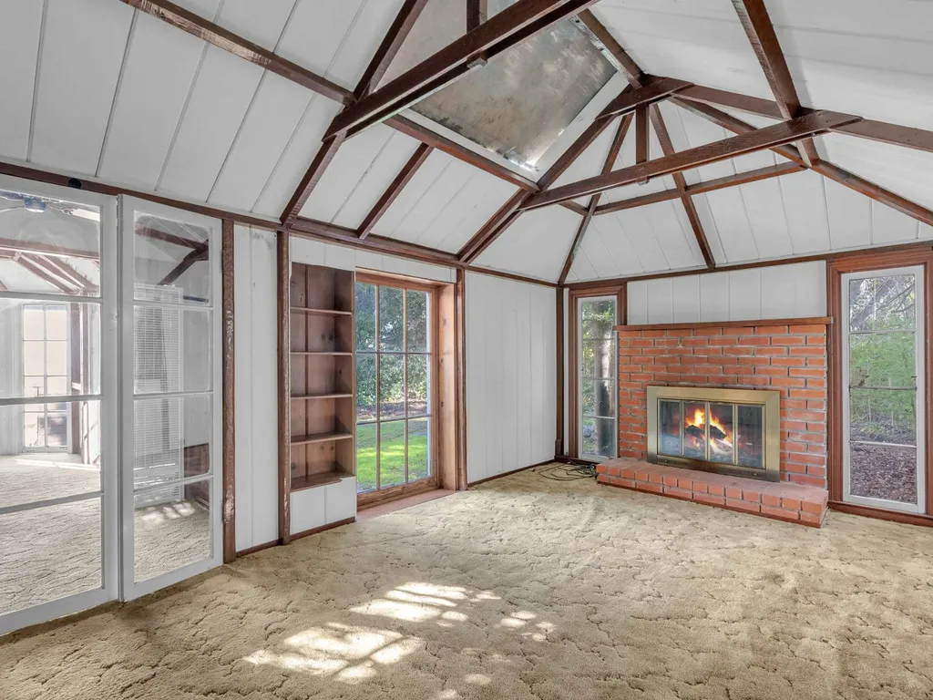 Room with exposed wood beams, a brick fireplace and glass doors to the garden