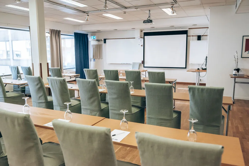 Ljus möteslokal i skolsittning med gröna stolar, whiteboard och stora fönster