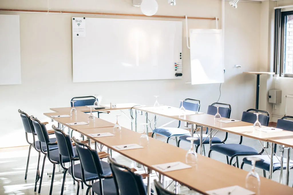 Grupprum med bord i U-form, blå stolar, whiteboard och blädderblock
