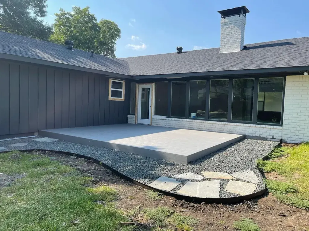 New concrete patio extension behind a house with a stone border