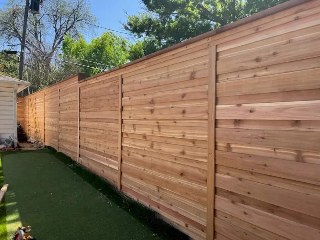 Tall horizontal cedar privacy fence along a side yard with artificial turf
