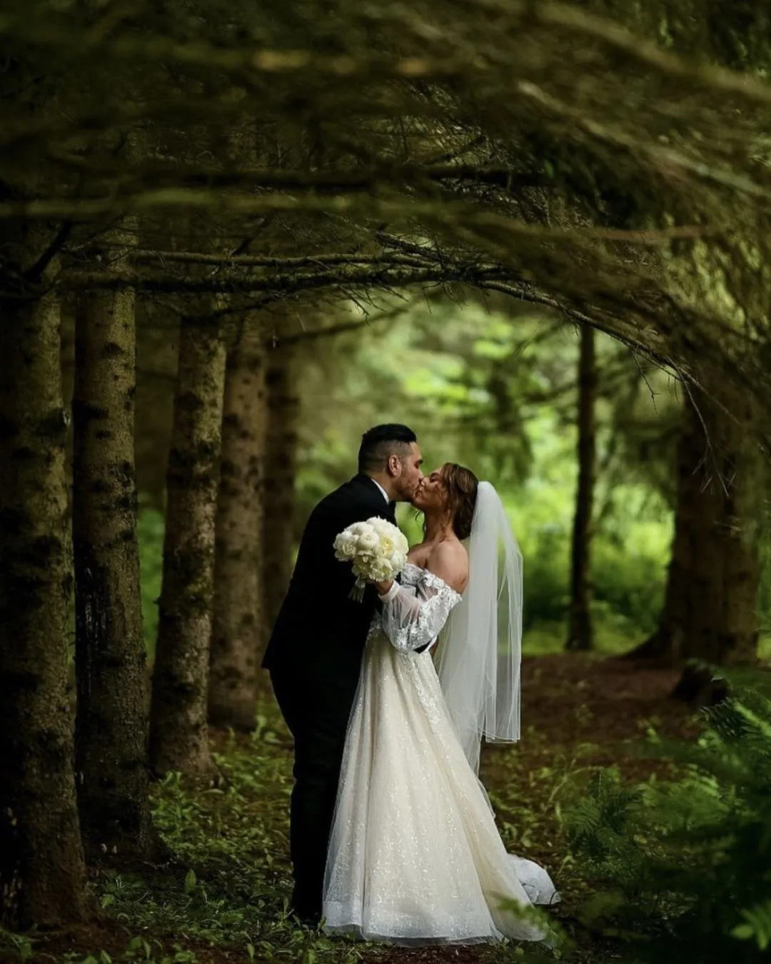 Couple kissing in a forest with a white bouquet