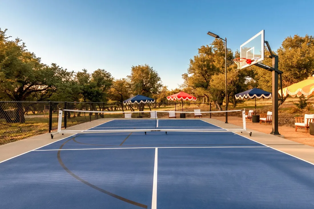 Multi-use court with a basketball goal, pickleball net and scalloped umbrellas on acreage
