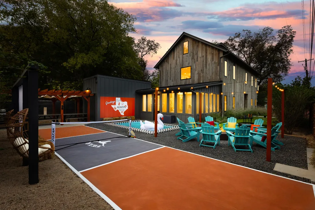 Pickleball court in orange and slate with pergola seating, plunge pool and fire pit lounge at a barn-style home