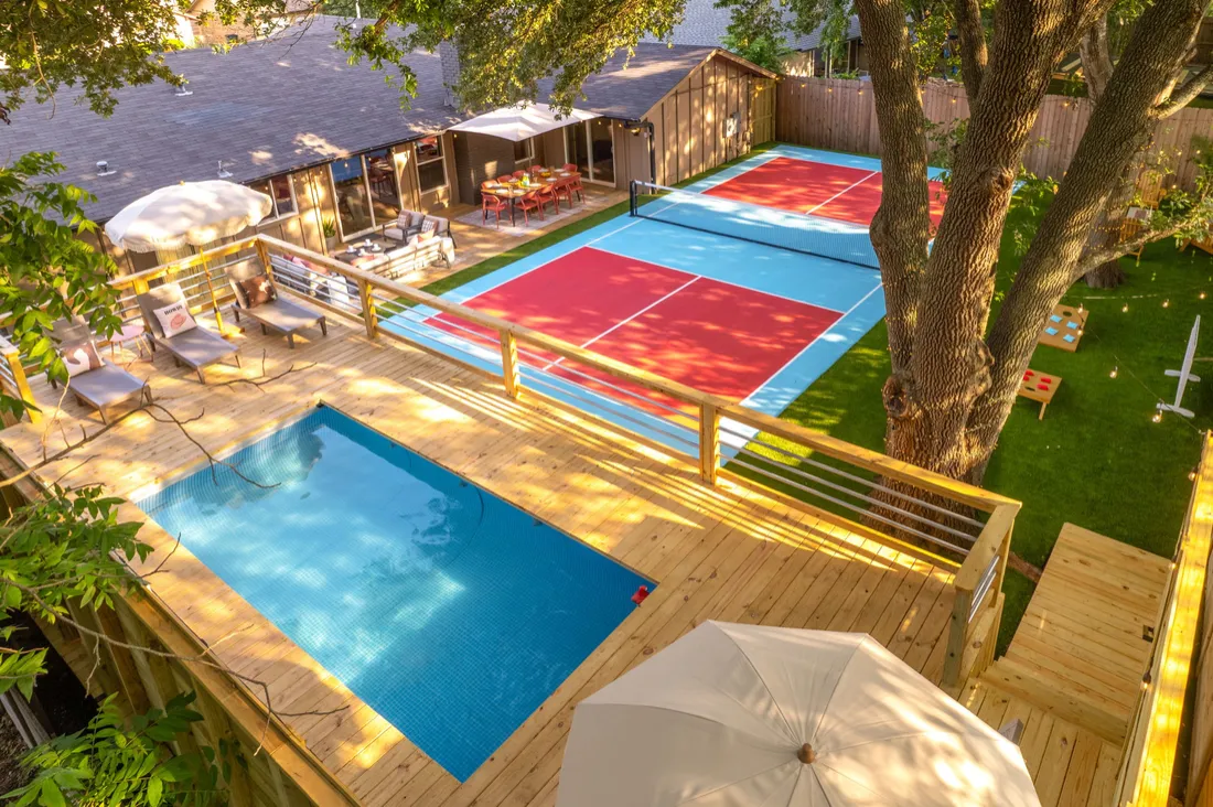 Pool, deck and pickleball court on a wooded lot, aerial