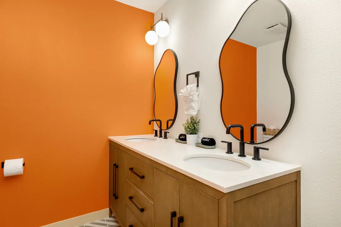 Bathroom with a double vanity, black fixtures and an orange accent wall