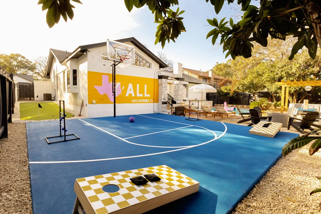 Blue half-court with a checkered cornhole board and a painted Y'ALL mural, San Antonio