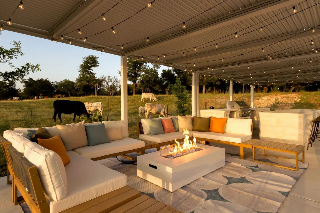 Lounge with a fire table under a steel pergola, cattle grazing beyond, Fredericksburg