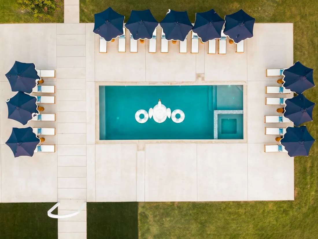 Pool and spa ringed by loungers and navy umbrellas, aerial