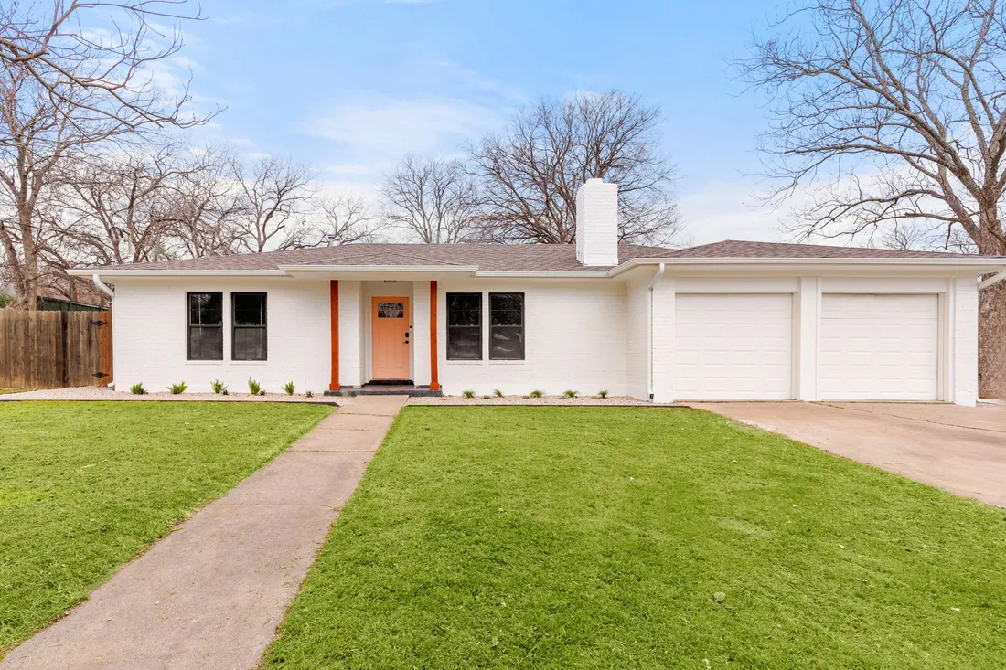 Ranch exterior in painted white brick with an orange front door