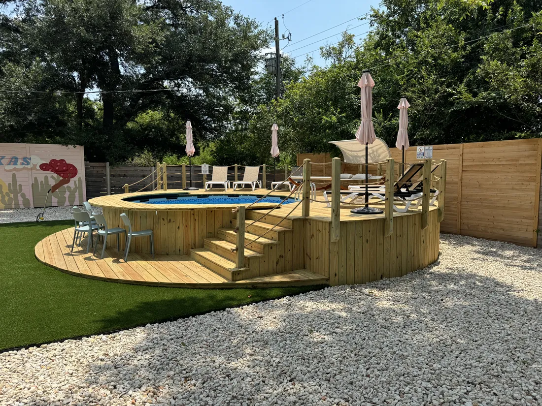 Above-ground pool wrapped in a round wood deck with stairs, loungers and umbrellas