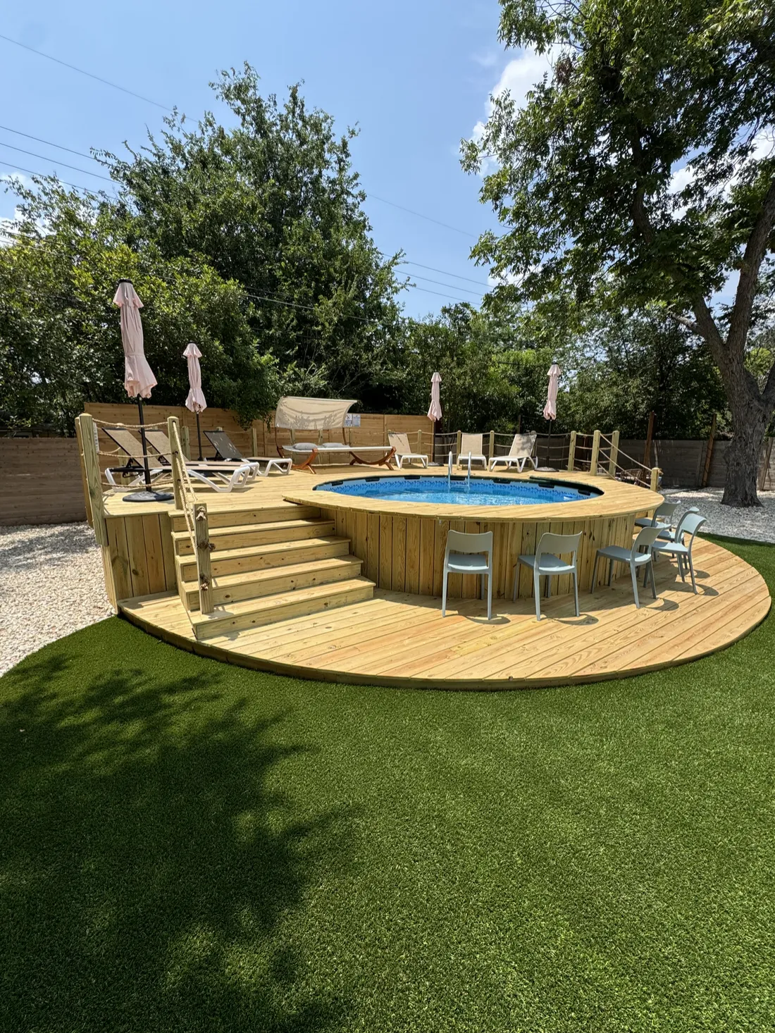 Round wood pool deck with built-in stairs and bar seating on artificial turf