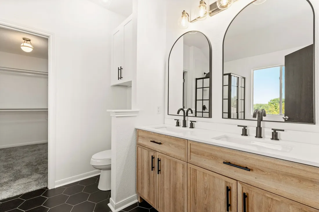 Bathroom with arched mirrors, a double wood vanity and black hex tile