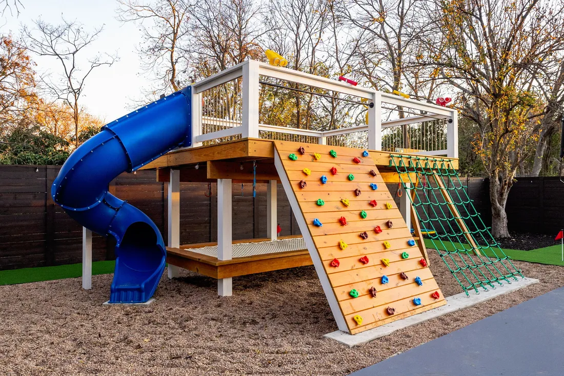 Raised play deck with a climbing wall, cargo net and spiral slide