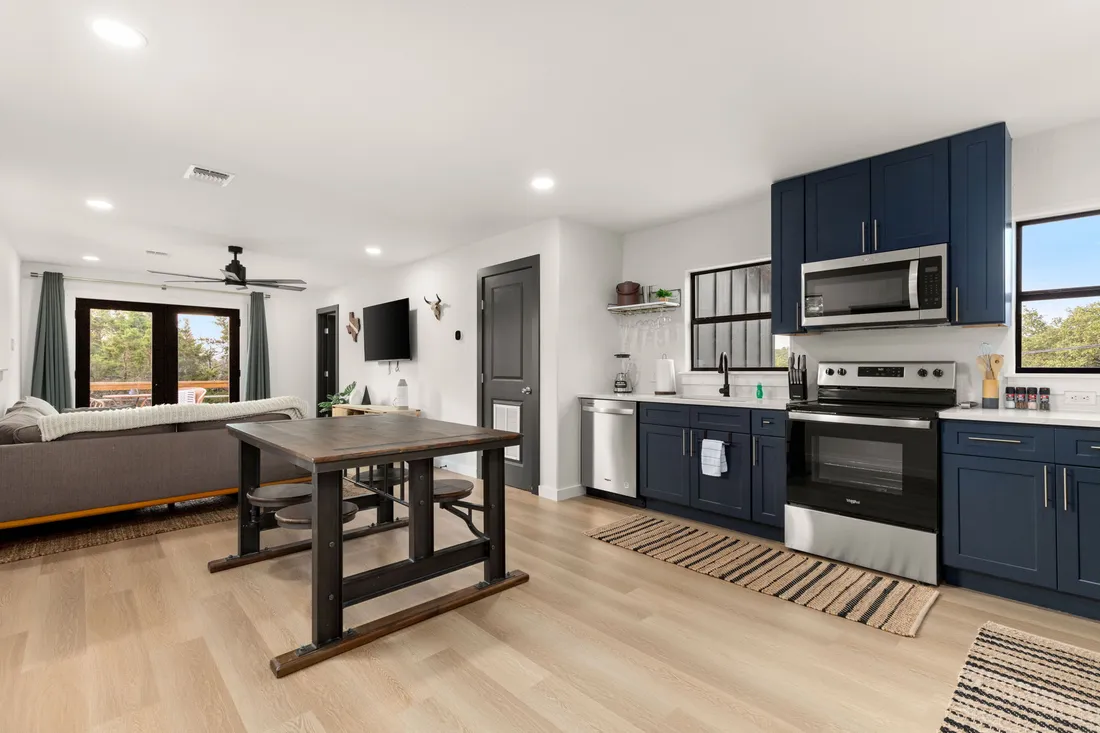 Open kitchen and dining with navy cabinets, stainless appliances and plank flooring