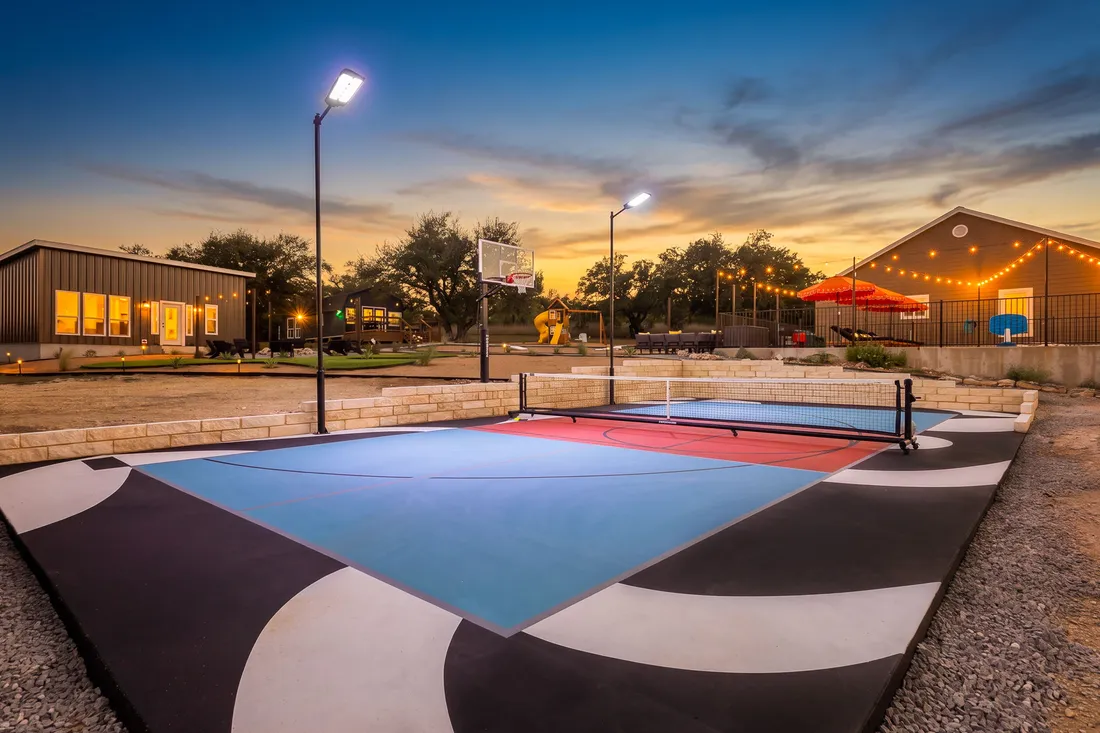 Pickleball court in blue and red with a painted black and white surround and court lights at dusk