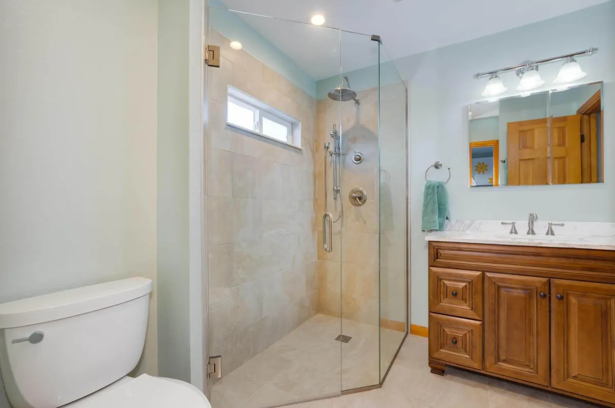 Acoma Drive Bath main photo — Bathroom remodel with walk-in tile shower, frameless glass, and wood vanity with quartz counter.