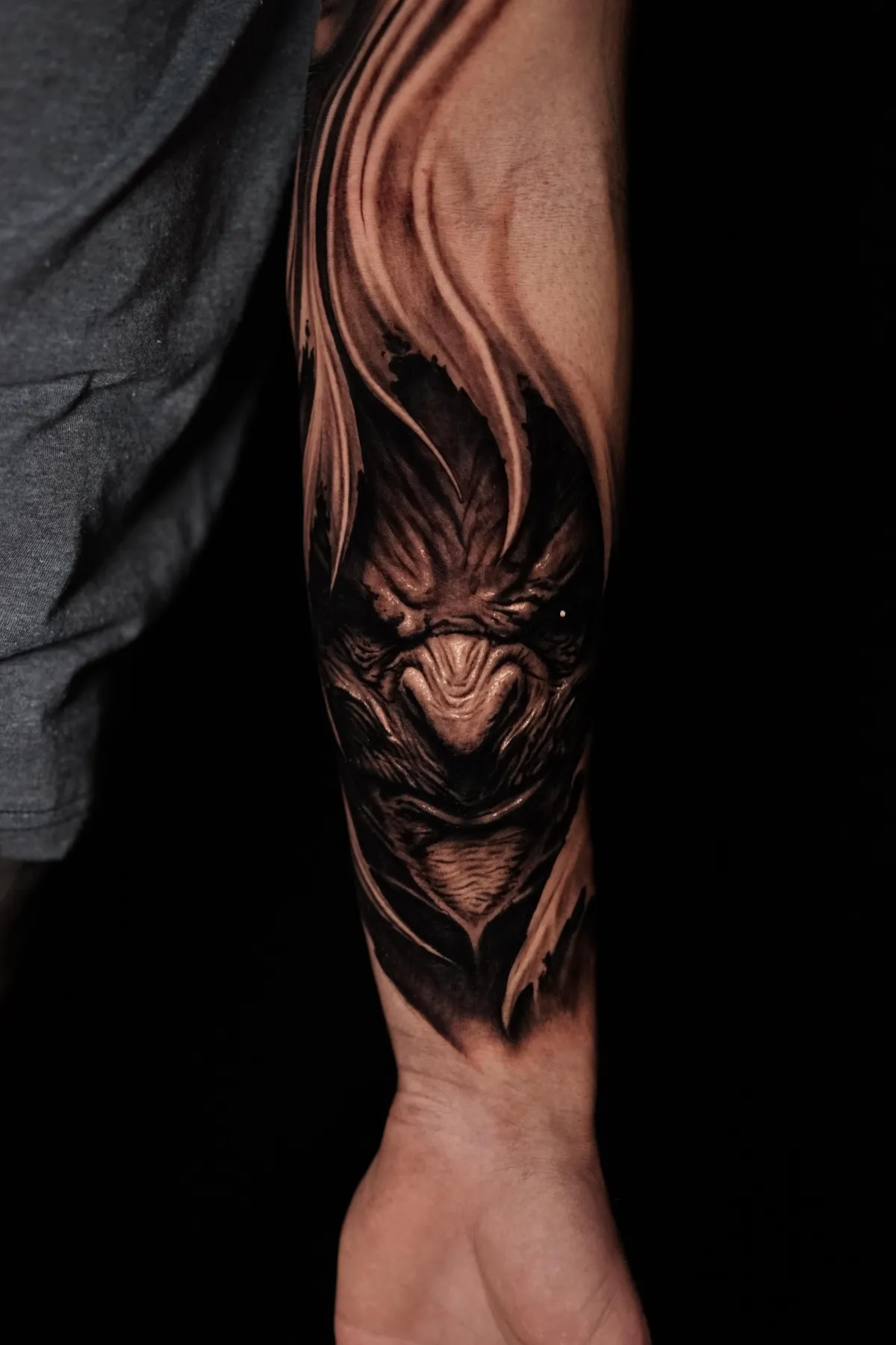Dark black and grey creature tattoo with dramatic shadow, flowing shapes and intense facial detail by James Strickland in Missoula Montana