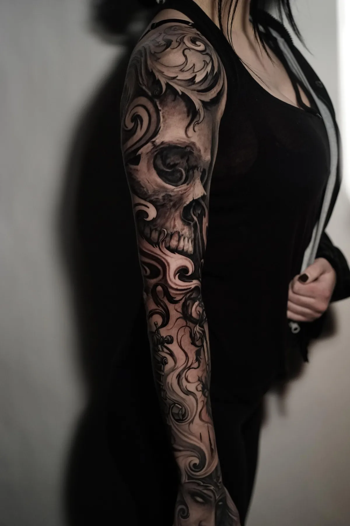 Black and grey sleeve tattoo featuring a skull surrounded by sweeping ornamental forms and dark realism shading by James Strickland in Missoula Montana