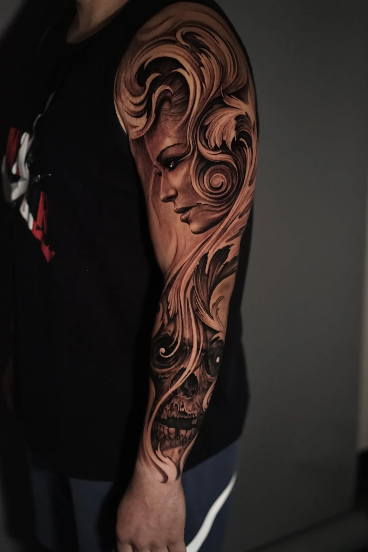 Black and grey realism sleeve combining a stylized female portrait, flowing forms and skull imagery by James Strickland in Missoula Montana