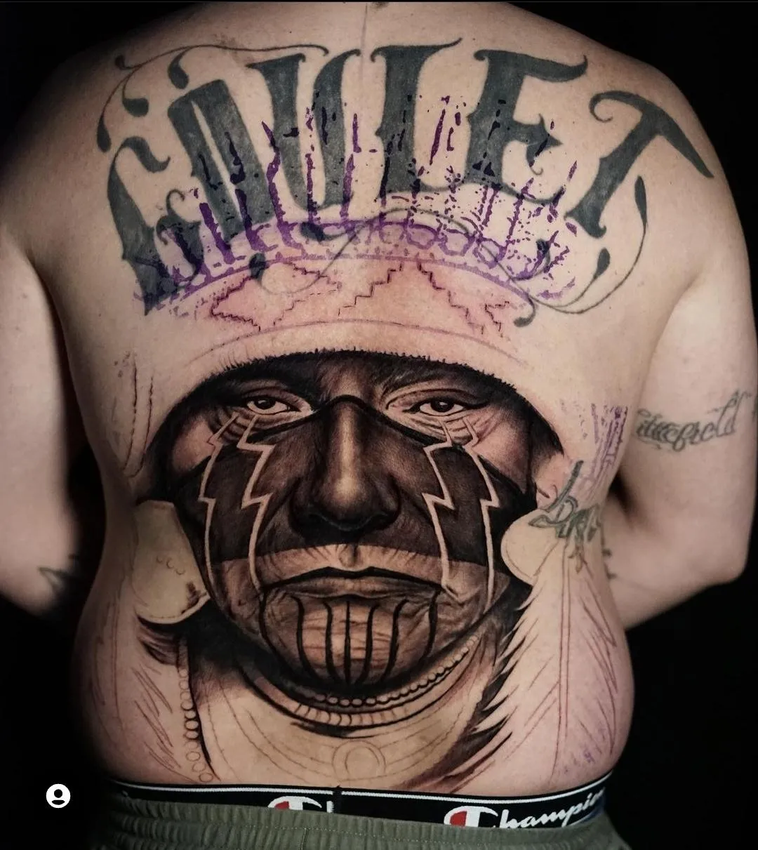 Large black and grey Native warrior back tattoo with bold facial markings and lettering by James Strickland in Missoula Montana