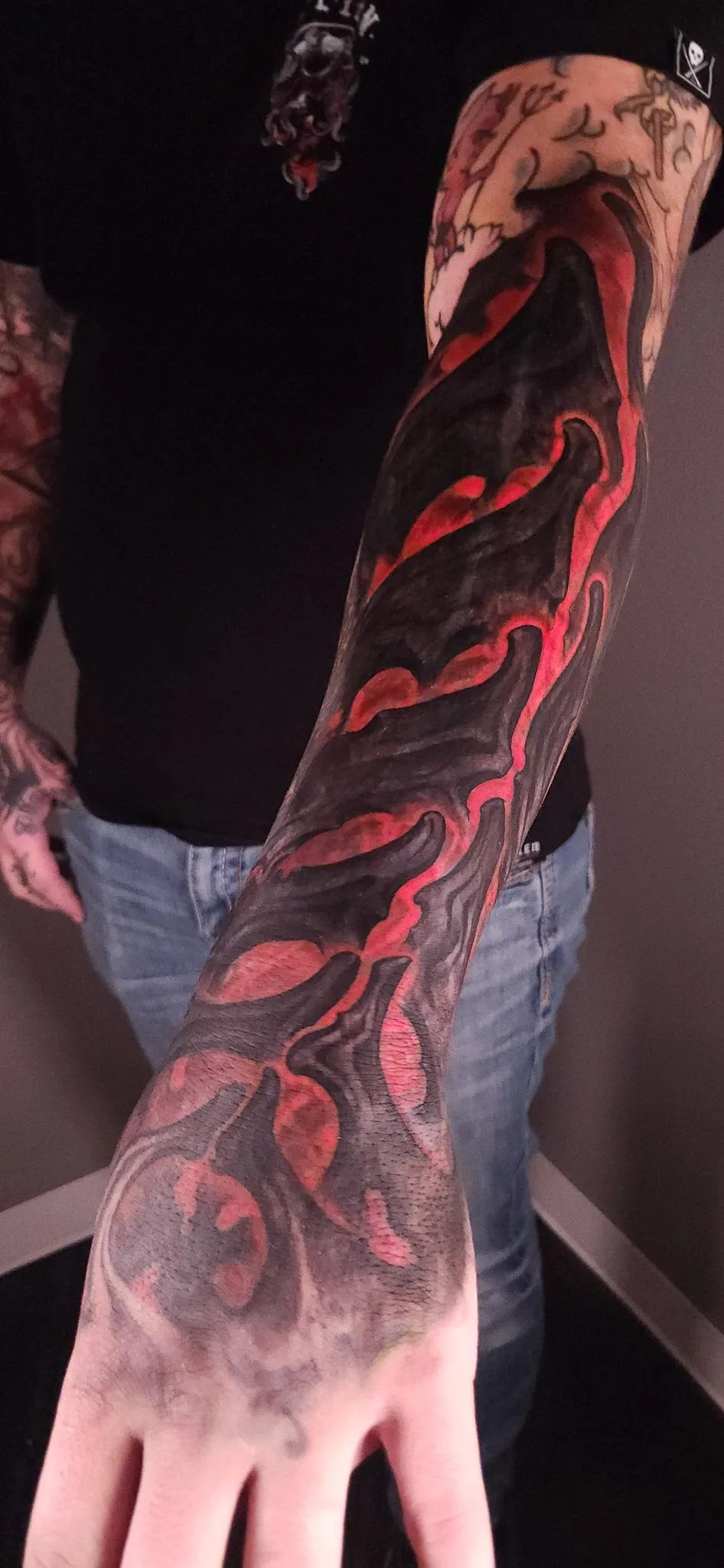 Red and black abstract forearm tattoo with flowing organic shapes by Mickey Schlick