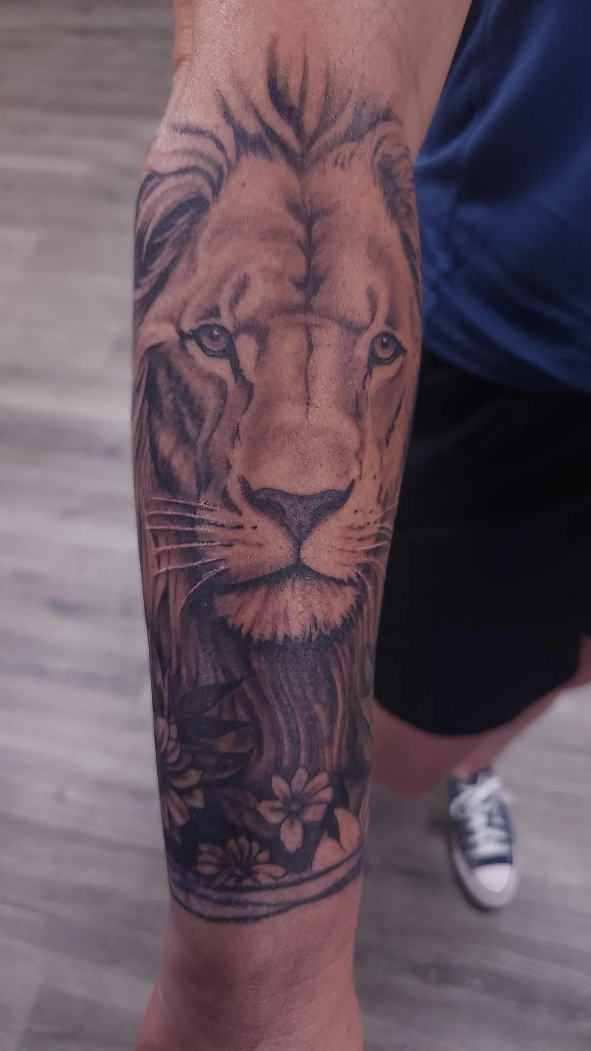 Black and grey lion portrait forearm tattoo with floral details by Mickey Schlick
