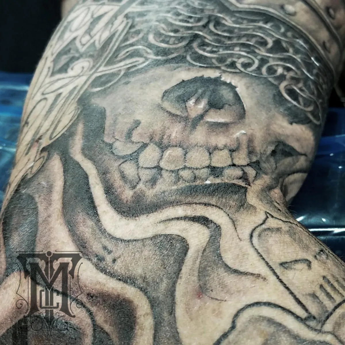 Black and grey skull tattoo with sweeping ornamental forms by Mickey Schlick