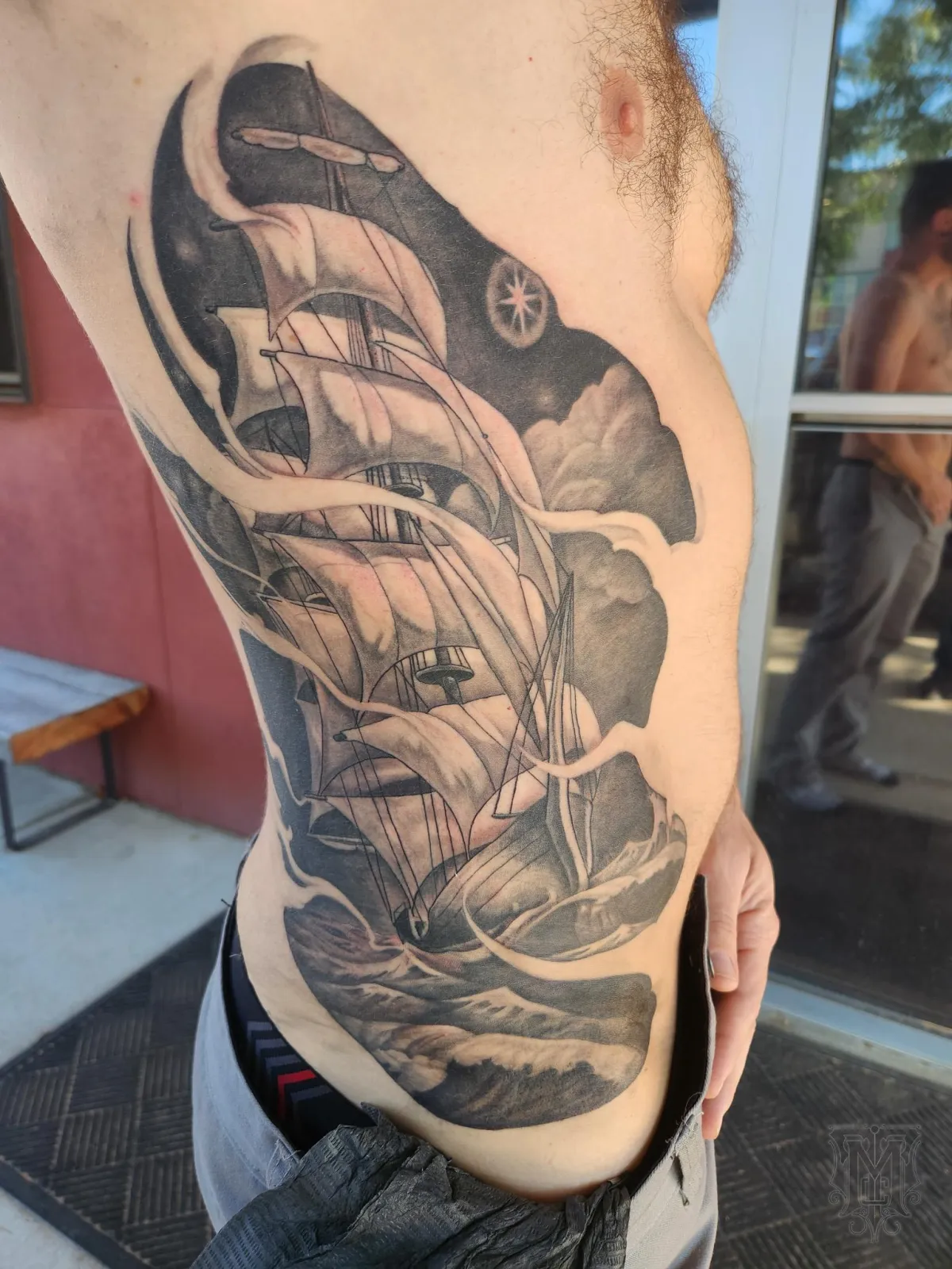 Large black and grey sailing ship tattoo with waves and clouds by Mickey Schlick in Missoula Montana