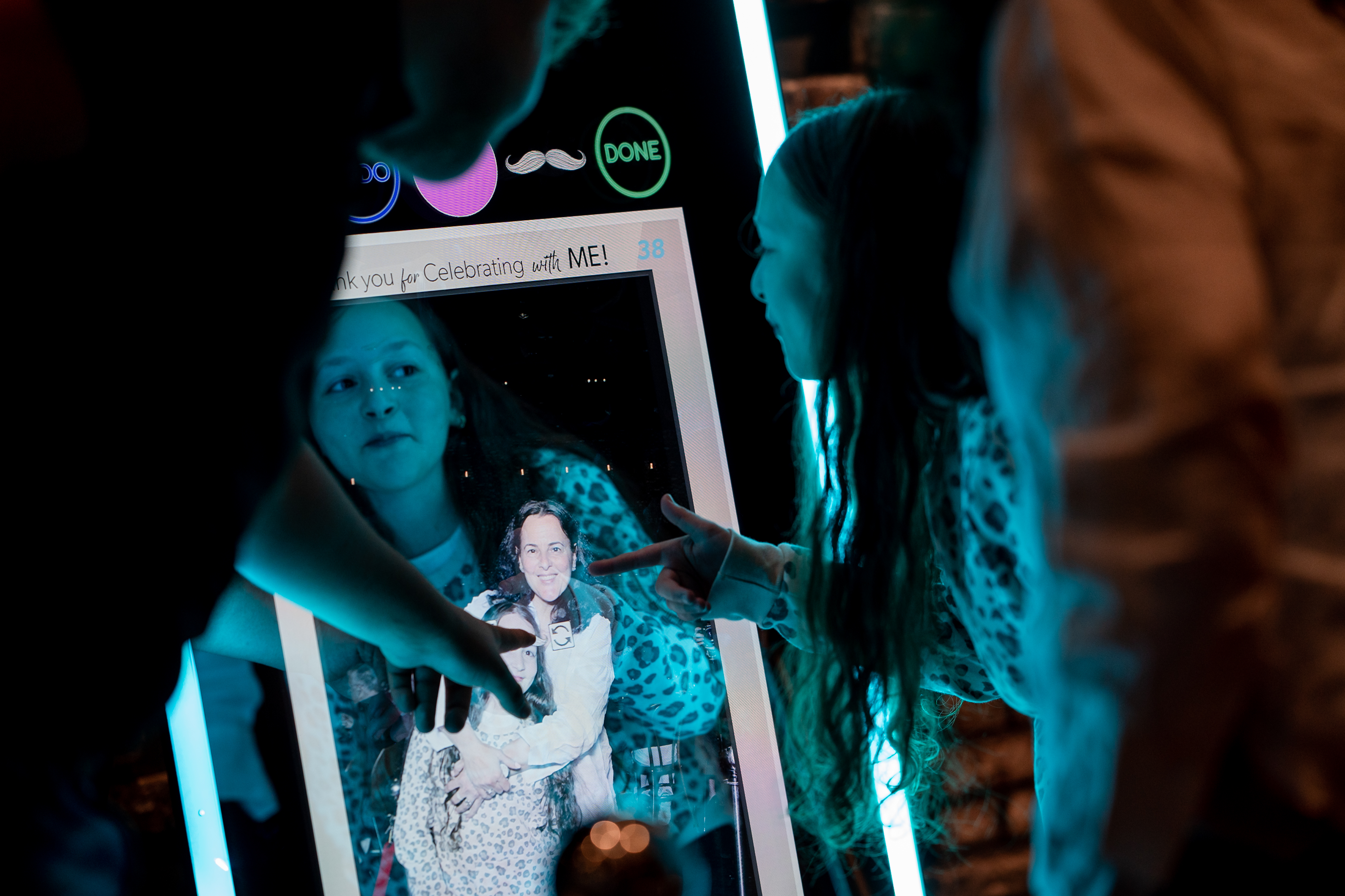 Woman interacting with glowing photo booth screen at night event – pointing to family photo of mom hugging daughter on display, with blue LED lights and 'Thank you for Celebrating with ME!' message in Chicago photo booth rental