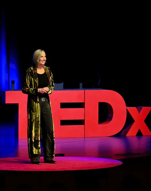 Image of Michelle Cameron Coulter standing on the TEDx stage with the TEDx text in the background