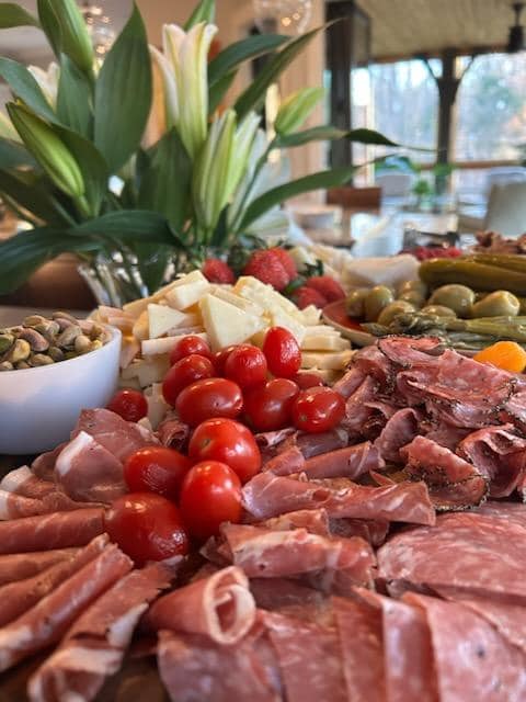 Elegant charcuterie grazing table with cured meats, cheeses, olives, cherry tomatoes, and fresh flowers by Foodie Call catering services