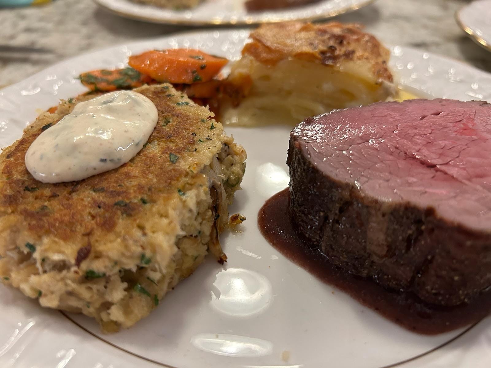 Surf and turf plated dinner with steak, crab cake, and roasted vegetables by Foodie Call private chef services