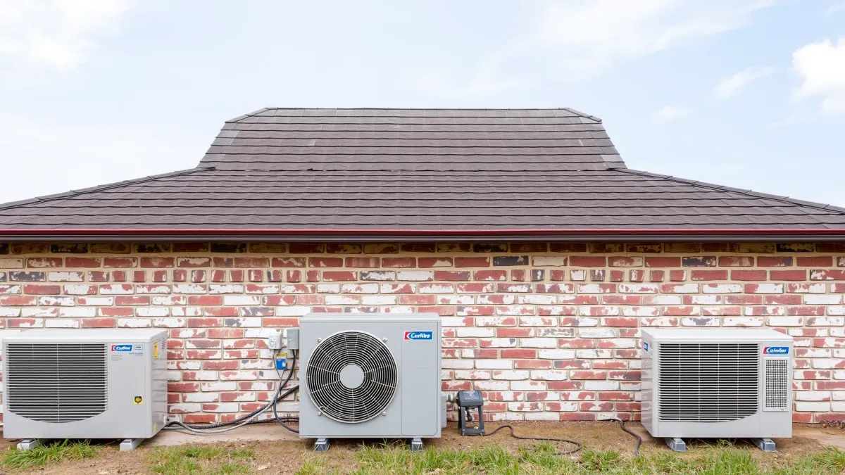 Well-maintained outdoor air conditioning unit with polished fins, refrigerant lines, and branded components in a sunny, green residential setting.