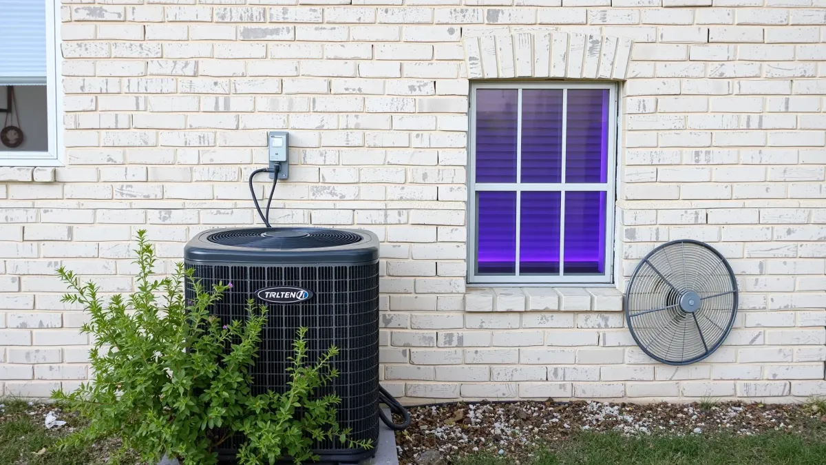 Outdoor modern air conditioning unit on concrete pad in Texas backyard with green grass, trees, and blue sky.