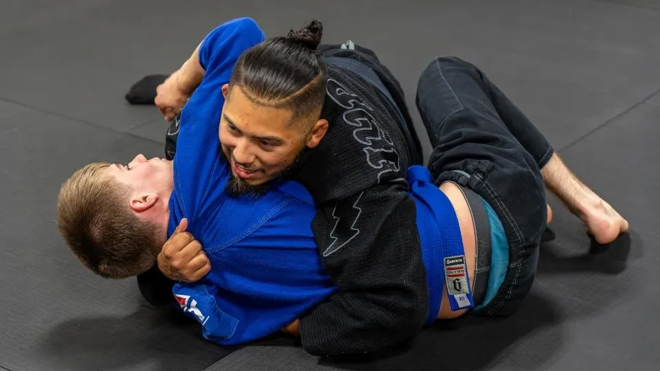 Professor Alec Flores, Head Coach at Mountain Rollers Jiu-Jitsu in Colorado Springs, demonstrates a grappling technique during an evening Brazilian Jiu-Jitsu gi class. With a focus on control and technique, Professor Flores provides hands-on guidance to students, enhancing their skill development in a supportive and disciplined environment. Mountain Rollers Jiu-Jitsu is a premier BJJ gym in Colorado Springs, offering expert instruction for students of all levels.